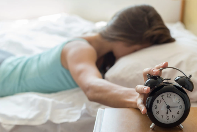 A person reaching out to turn off a black alarm clock while lying in bed.