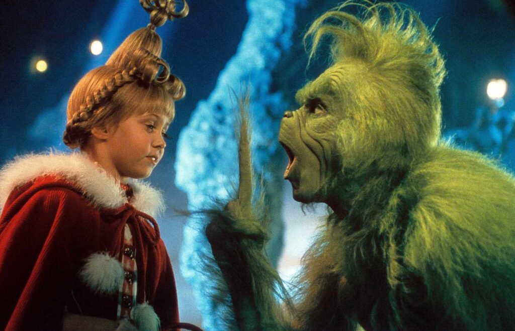 A young girl in a red costume engages with a green, furry character in a snowy, fantastical setting.