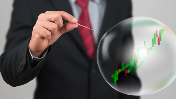 A person in a suit holding a pin to a bubble with a stock market growth chart inside it.