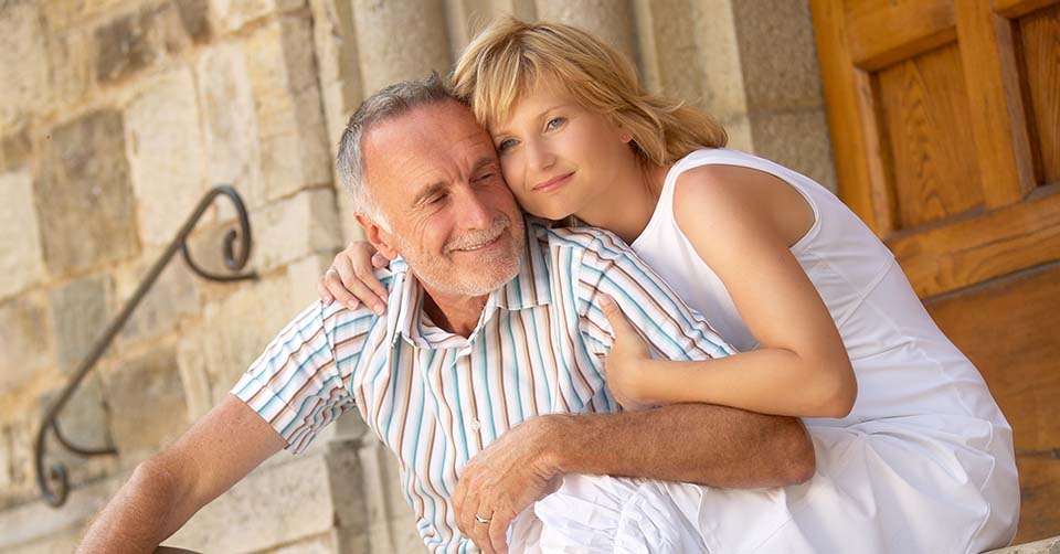 A joyful couple sharing an affectionate moment outdoors, with a scenic stone background and warm smiles.