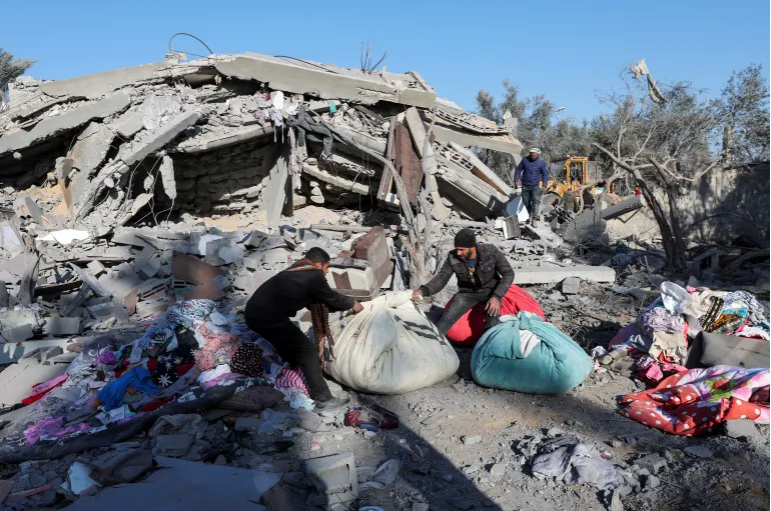 Palestinians collect belongings at the site of an Israeli strike on a house in Deir el-Balah in the central Gaza Strip [Ramadan Abed/Reuters]