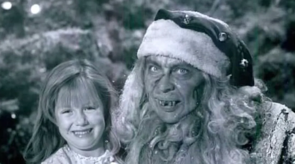 Tales from the Crypt: And All Through the House (1989): A black and white image showing a smiling young girl alongside a character in fantastical makeup and costume resembling an old witch or mythical creature.