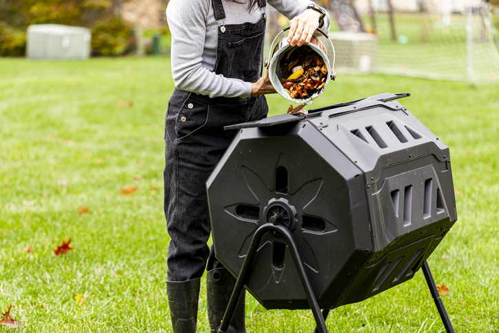 Transforming Kitchen Scraps into Nutrient-Rich Compost 3 A person pouring organic waste into a compost tumbler in a grassy yard.