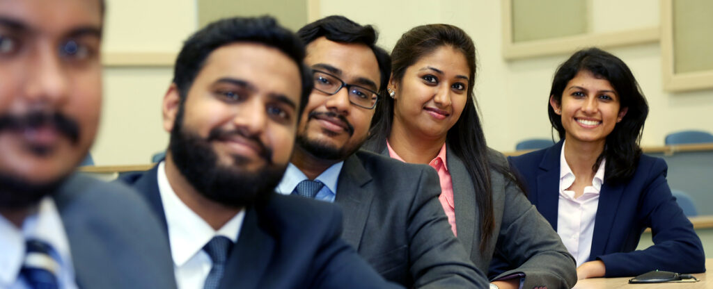 A diverse group of five professionals smiling and posing together in a business setting, showcasing teamwork and collaboration.