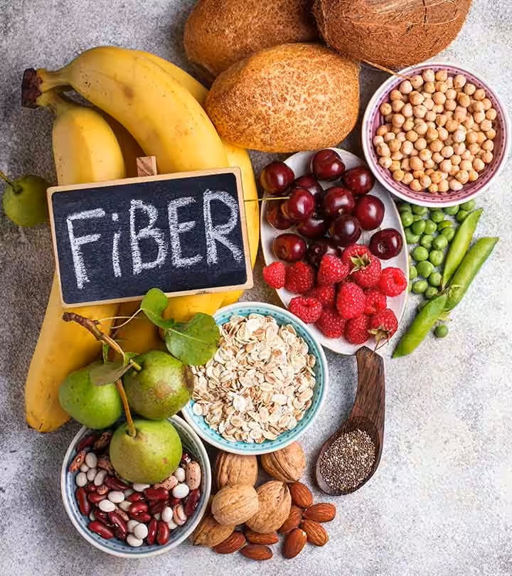 15 Research-backed methods for losing weight without exercise 9 A colorful assortment of fiber-rich foods including bananas, coconuts, various fruits, legumes, nuts, and oats, with a chalkboard sign reading "FIBER."