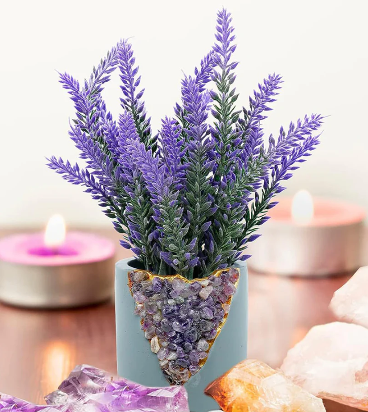 A vibrant lavender plant in a crystallized pot, surrounded by glowing candles and crystals on a wooden surface.