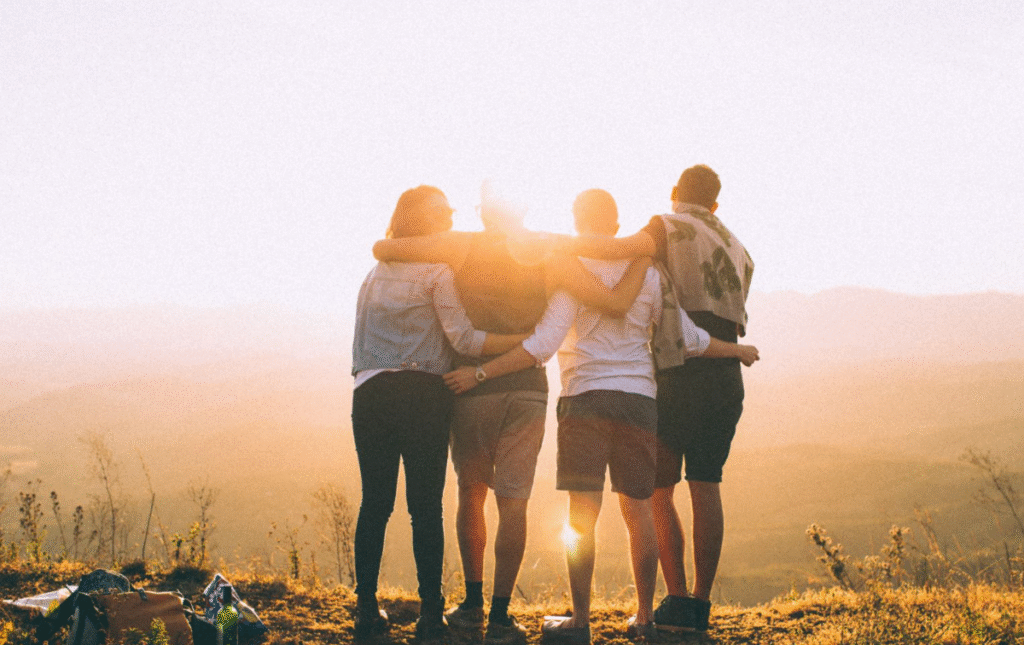 10 Habits of Successful People You Can Begin Practicing Today 8 A group of four friends standing together, embracing each other against a scenic sunset backdrop, creating a sense of unity and friendship.
