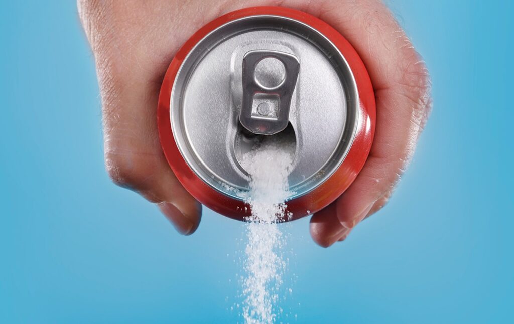 15 Research-backed methods for losing weight without exercise 7 A hand holding a soda can with sugar being poured out against a blue background, highlighting the sugar content in beverages.