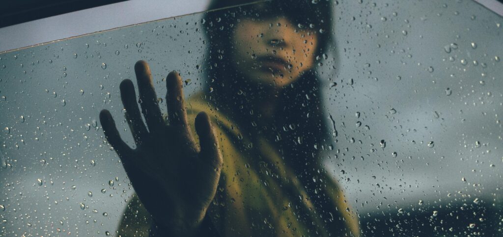Struggling with Overthinking? 5 A figure with a hand pressed against a rain-soaked window, evoking feelings of longing and introspection.