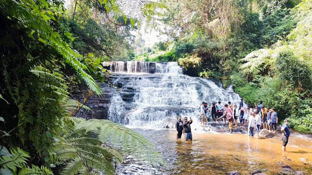 Hippie Trails in India That Promise a Journey to Freedom 10 A serene waterfall surrounded by lush greenery, with people enjoying the cool water at its base.