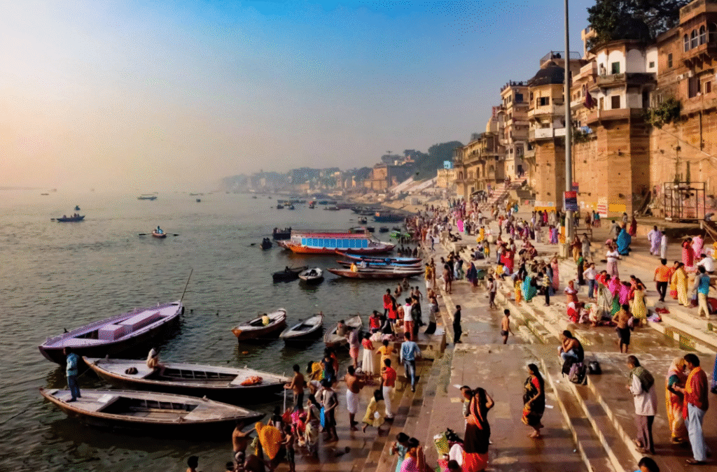 Hippie Trails in India That Promise a Journey to Freedom 5 A vibrant scene at the Ganges River in Varanasi, India, featuring people gathering along the steps, various boats on the water, and historical buildings lining the shore under a hazy sky.