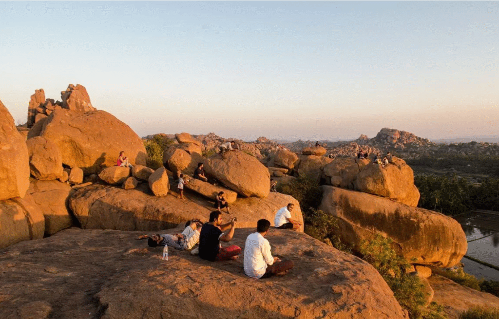 Hippie Trails in India That Promise a Journey to Freedom 8 People relaxing and enjoying the sunset on large boulders with a scenic backdrop of hills and fields.