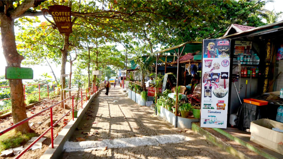 Hippie Trails in India That Promise a Journey to Freedom 9 A vibrant walkway lined with trees and local shops leading to a cozy coffee spot, featuring colorful signage and welcoming atmosphere.
