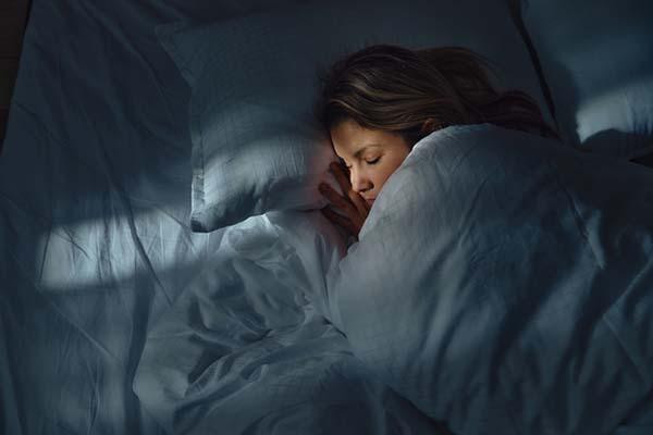 Woman peacefully sleeping under a white duvet, with soft light casting shadows on the bedding.