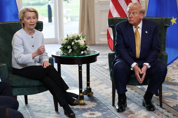Ursula von der Leyen speaks while Donald Trump listens during a discussion, with flags of the USA and EU in the background.