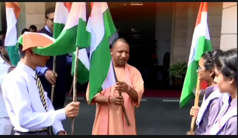 A group of students holding Indian flags and interacting with a leader outside a building during a patriotic event.