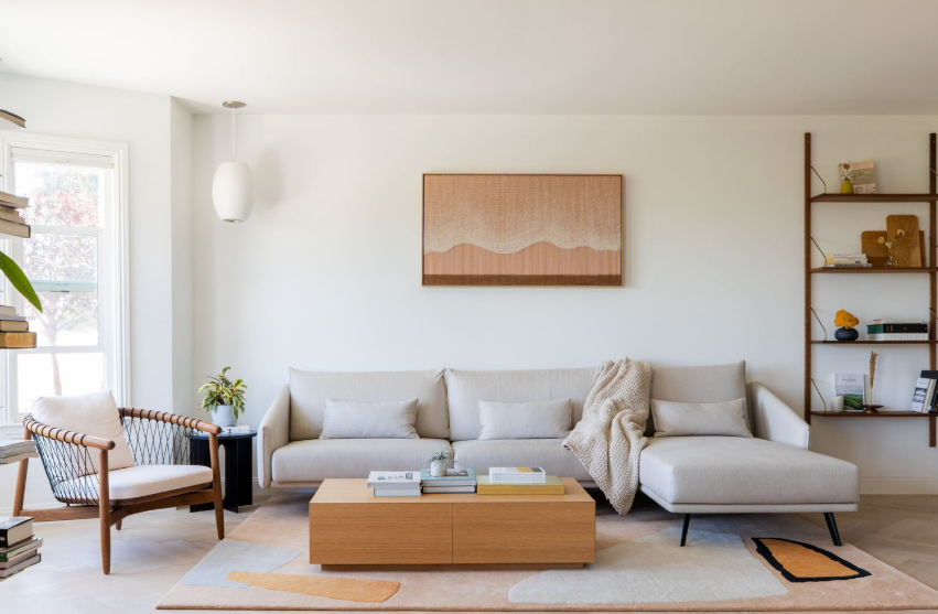 A serene living room featuring a light-colored sofa, minimalist decor, and a stylish bookshelf, complemented by natural light and a contemporary artwork on the wall.