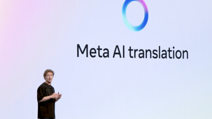 A speaker discussing Meta AI translation with the company logo displayed behind him on a large screen.
