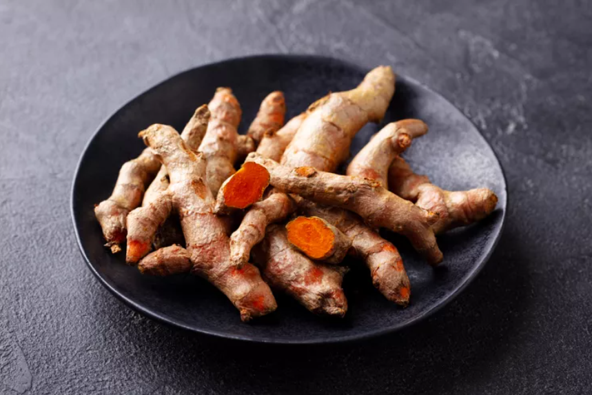 A close-up view of fresh turmeric roots on a black plate, showcasing their earthy texture and vibrant orange interior.