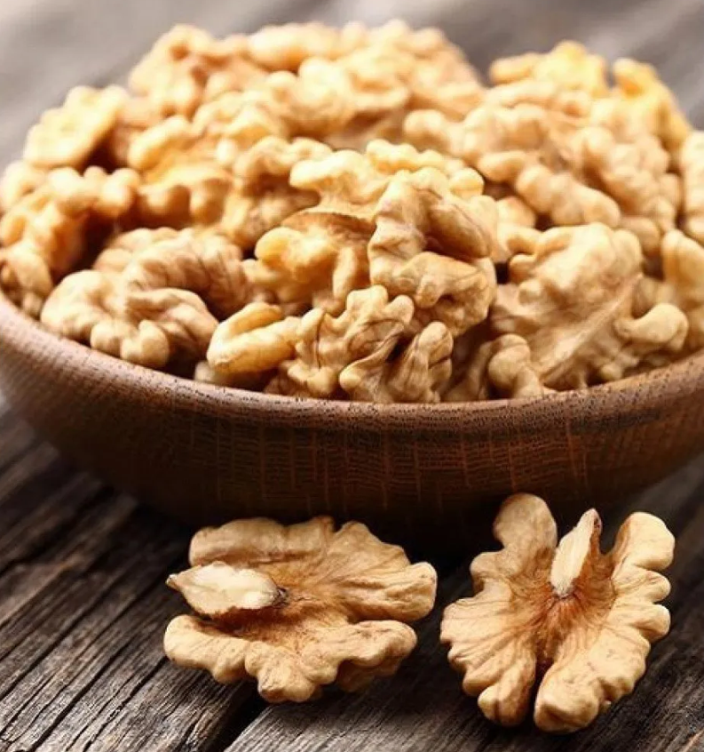 A close-up view of a bowl filled with shelled walnuts, with a few scattered pieces on a rustic wooden surface.