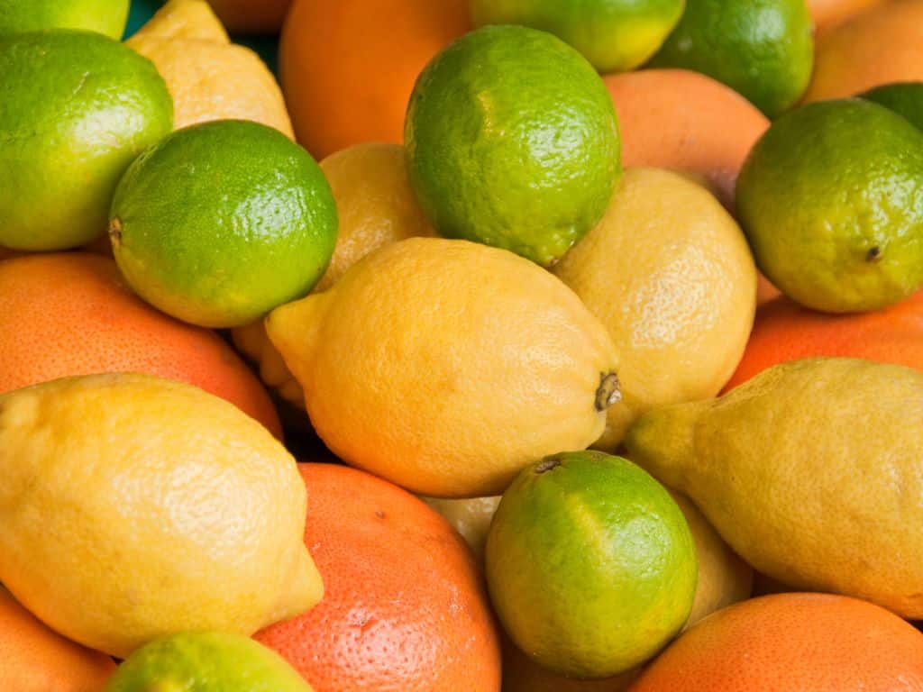 A vibrant assortment of fresh lemons and limes nestled among other fruits, showcasing their glossy skin and bright colors.