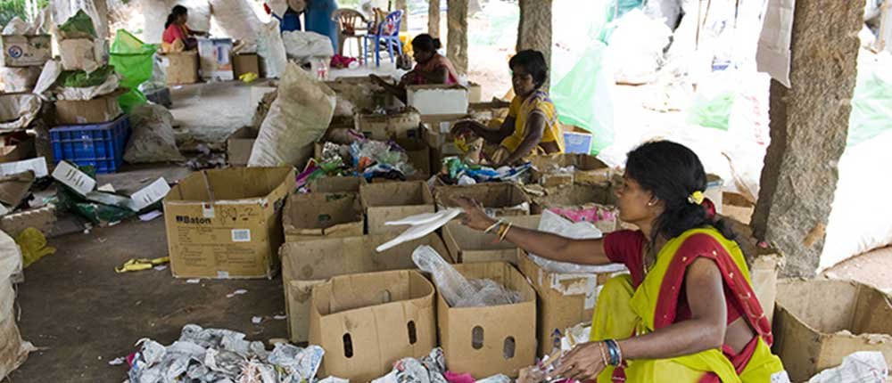 Women sorting through recyclable materials in a facility, surrounded by boxes and debris.