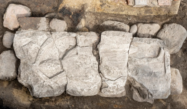 A close-up view of weathered stone artifacts with intricate carvings, partially embedded in earthy surroundings, showcasing archaeological findings.