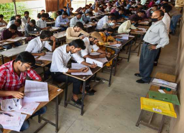 Students seated at desks taking an examination, with an invigilator overseeing the room.