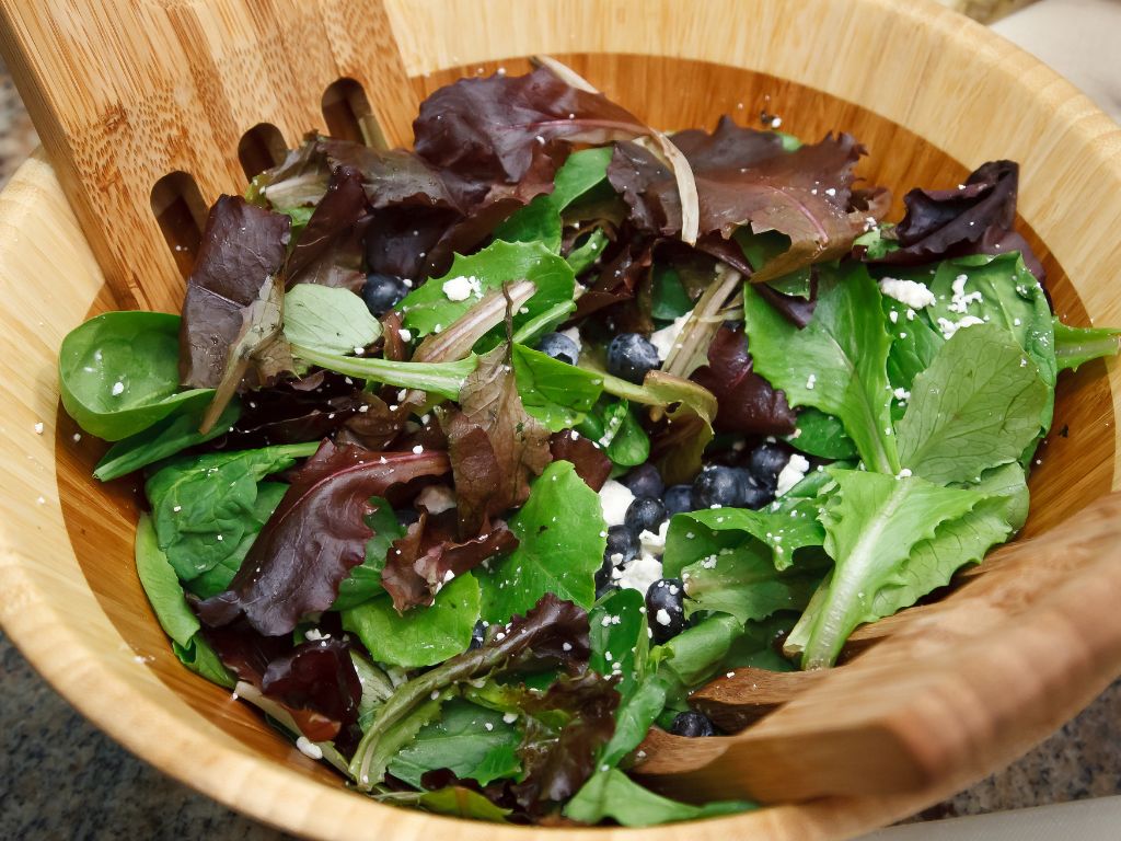A vibrant salad featuring a mix of leafy greens and blueberries in a wooden bowl, topped with feta crumbles.