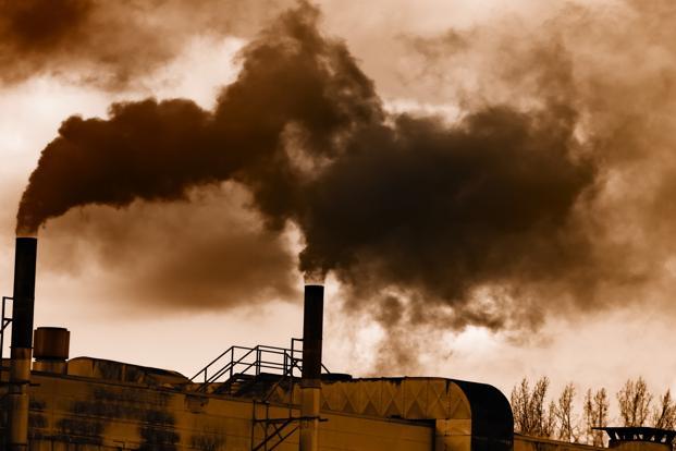 Thick dark smoke billowing from factory chimneys against a sepia-toned sky.