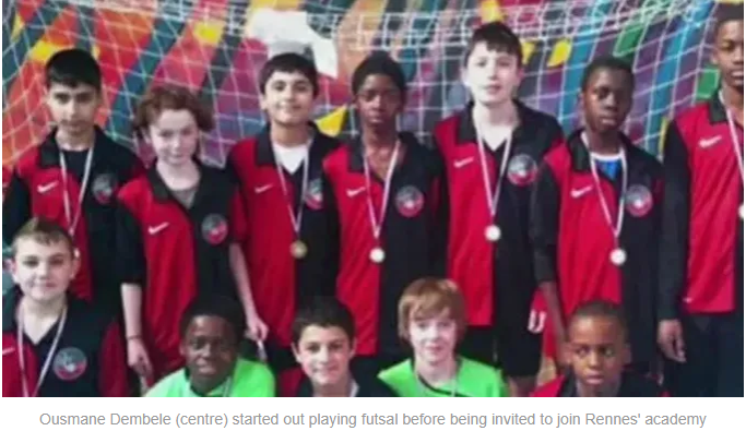 Group of young athletes in red and black jerseys with medals posing for a team photo in a colorful indoor sports setting.