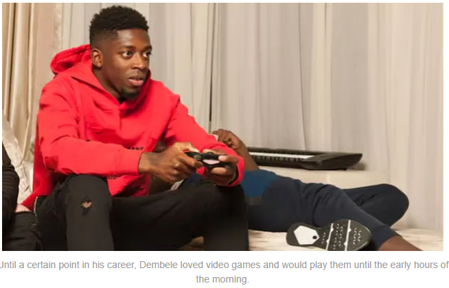 A young man in a red hoodie focused on playing video games, with another person lounging in the background.