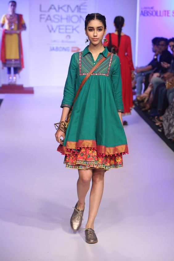 Model walking the runway in a vibrant green dress with colorful accents at Lakmé Fashion Week.
